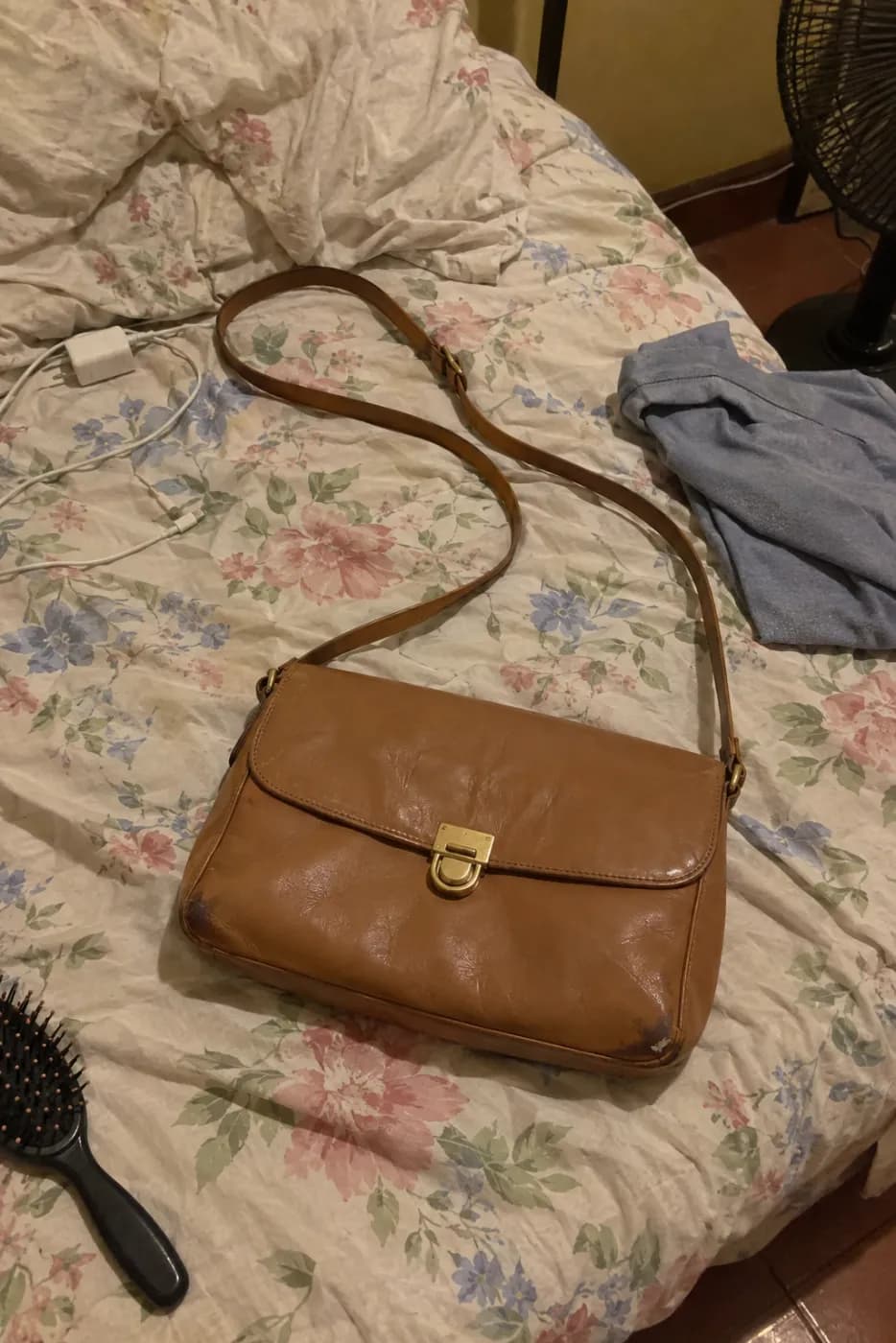Sample phone photo of a tan leather shoulder bag on an unmade bed, next to a charger cable, a t-shirt and a hairbrush