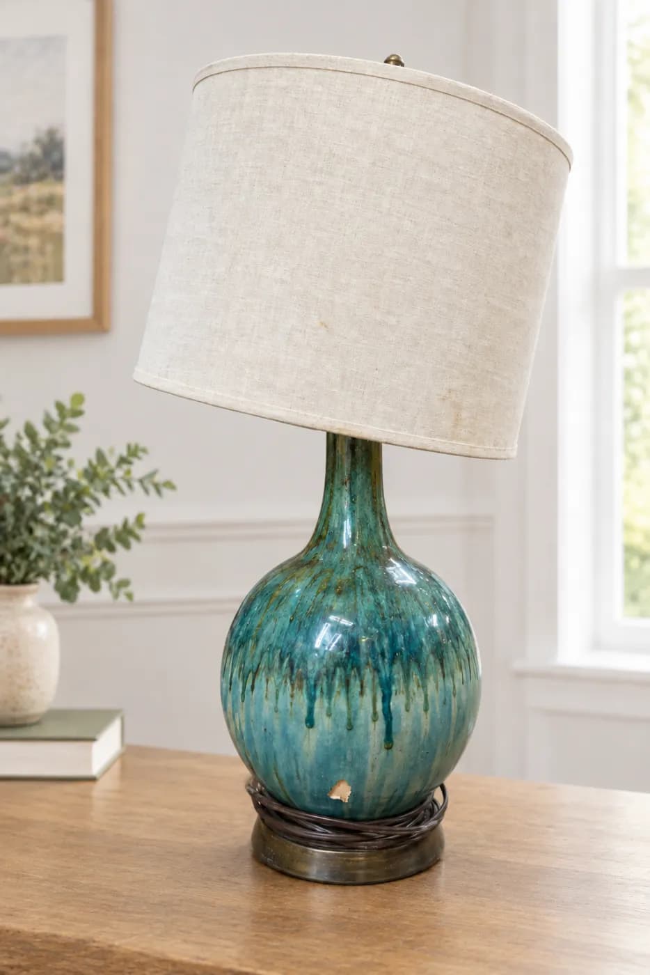The same lamp on a wooden table in a bright room, with the chip in its glaze still showing