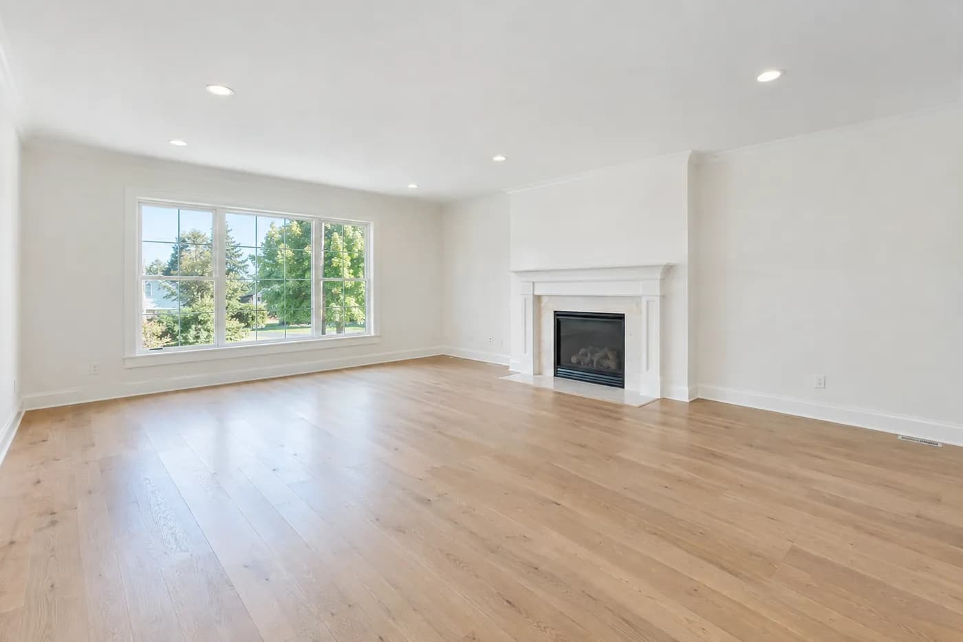 Sample photo of an empty living room with light oak floors, white walls, a large window and a fireplace